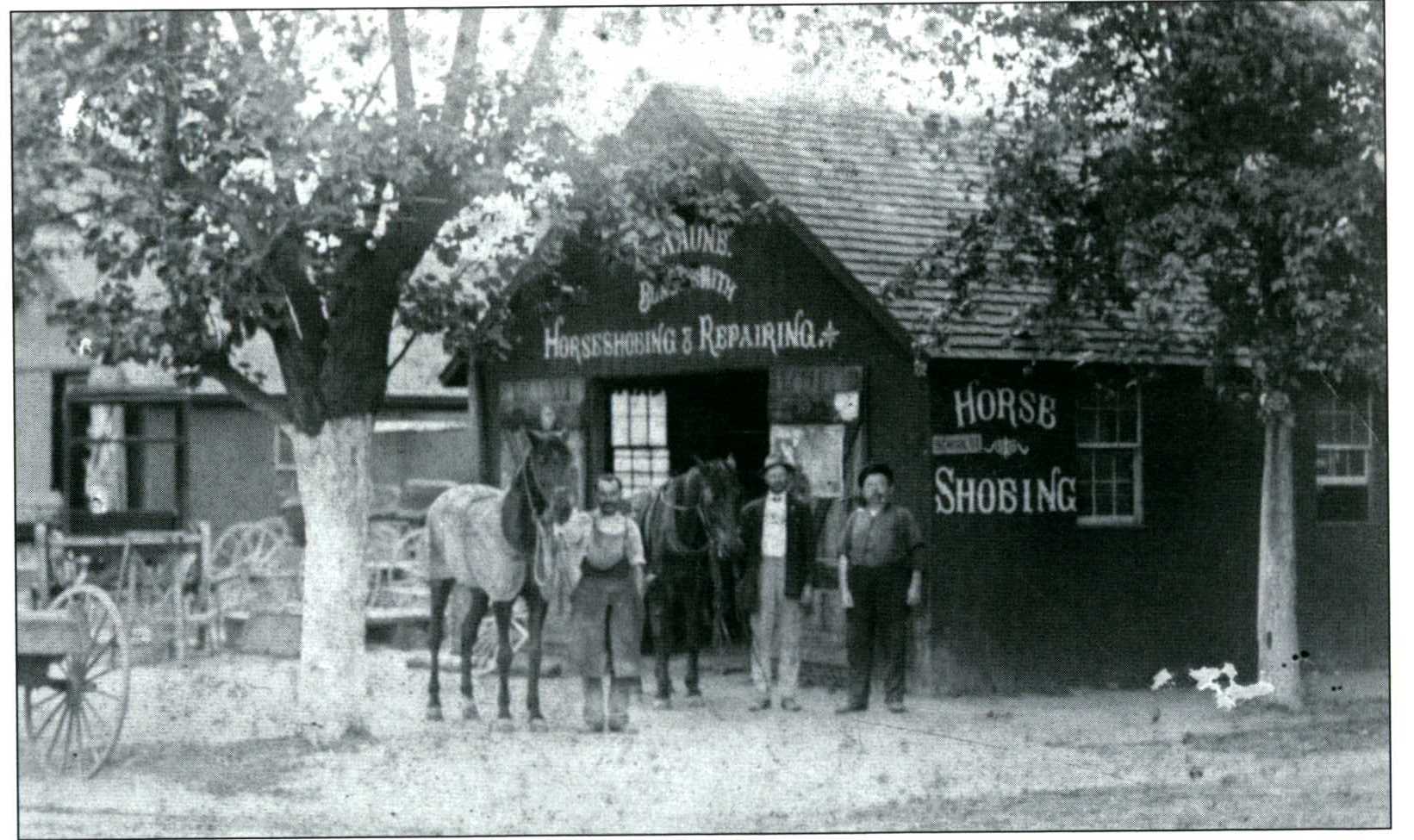 Black and white 19th century photo of men in front of blacksmith. 