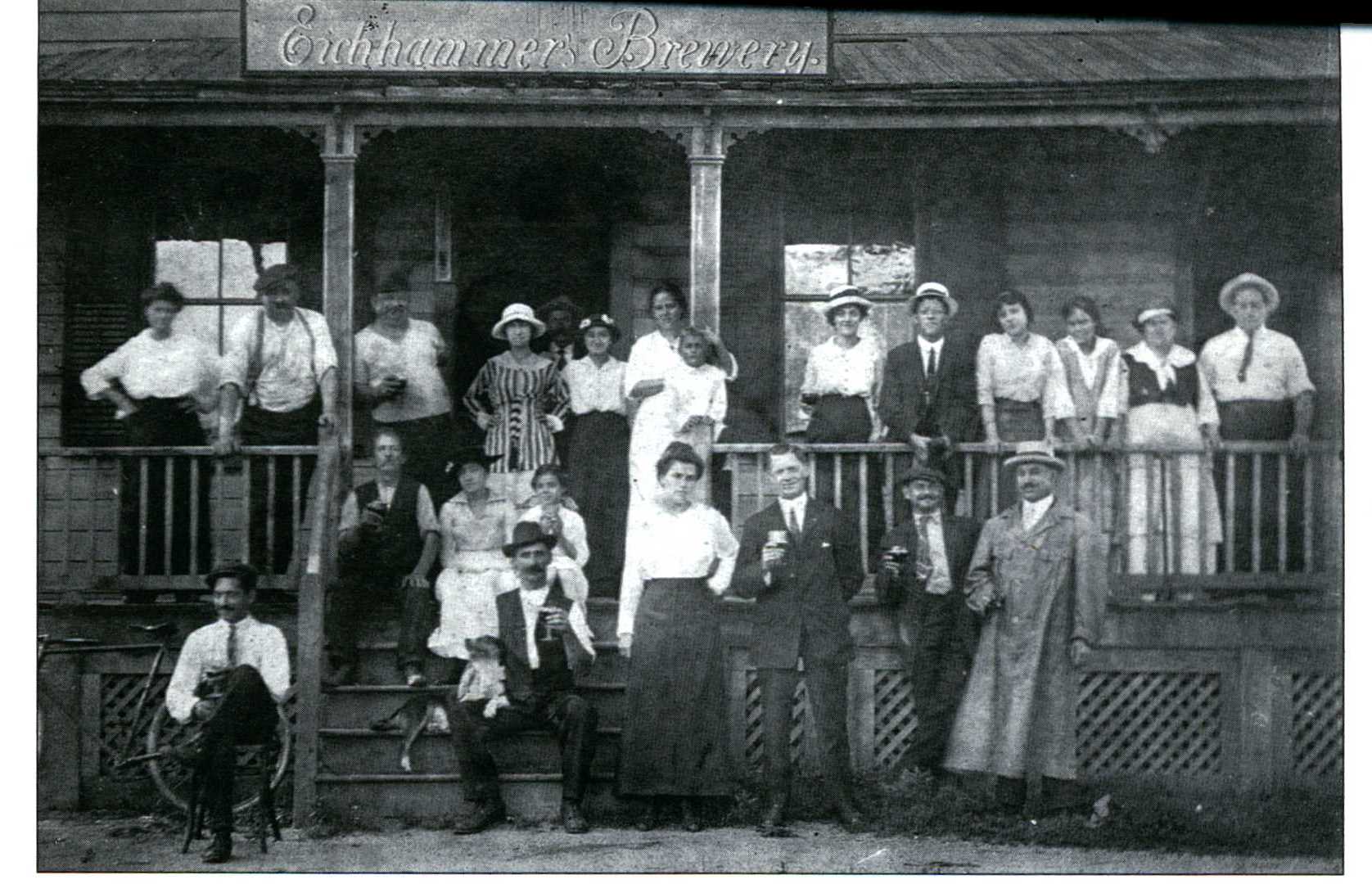 19th century black and white photo of men and women in front of brewery. 
