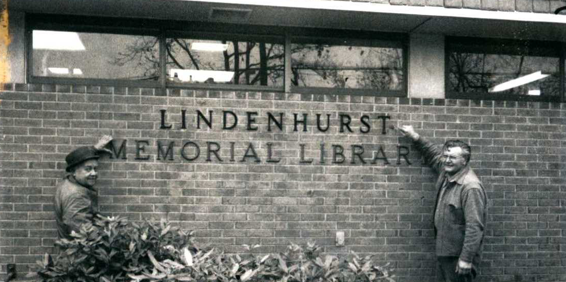 Two men standing next to the Lindenhurst Memorial Library sign