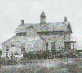 Black and white photo of completed school house with pupils in front. 