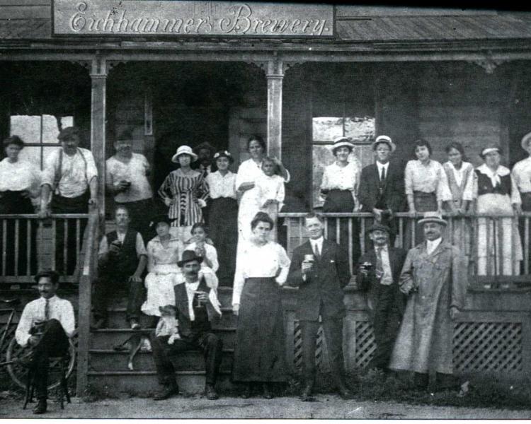 19th century black and white photo of men and women in front of brewery. 